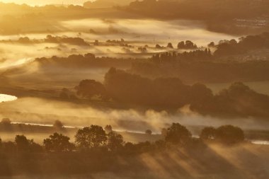 Morning sun rays over a haze-covered South Downs National Park clipart