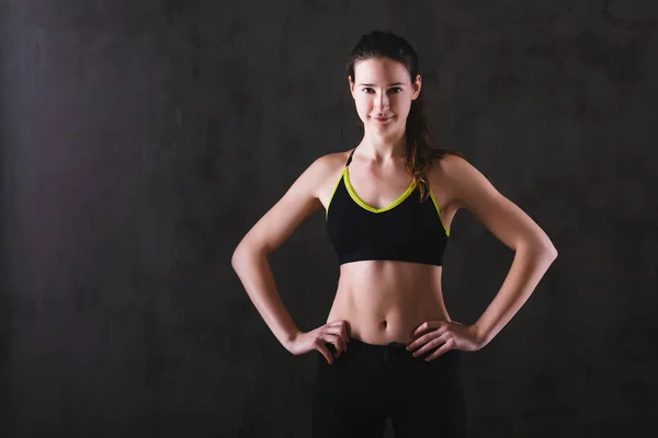 Fitness woman training in dark studio. Young girl posing on black background — Stock Photo, Image