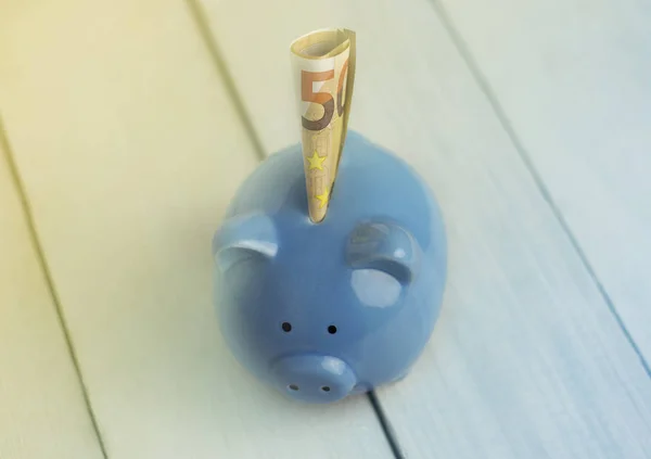 Blauwe spaarvarken met vijftig euro op een roze achtergrond. Symbool van storting, financiële zekerheid. Selectieve aandacht. — Stockfoto