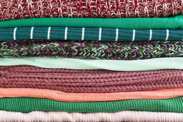 Close-up stack of folded colorful clothes. Background of different cozy clothes. Colorful fabric.