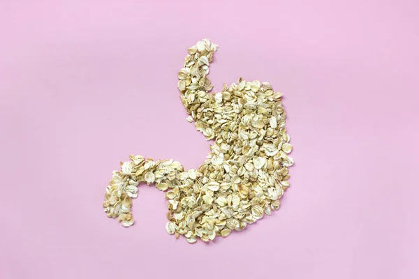 Oatmeal flakes in shape of stomach on pink paper background. Minimalistic concept of diet and healthy eating. Closeup horizontal image in top view with copy space.