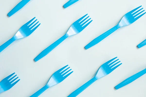 Many blue plastic forks on light background, top view. Disposable tablewear, sorting plastic concept. Creative pattern, flat lay