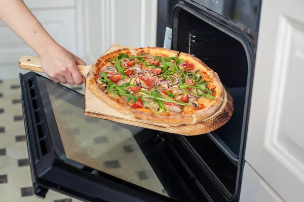 Close-up. Vrouw hand zet pizza in de oven. Stockfoto