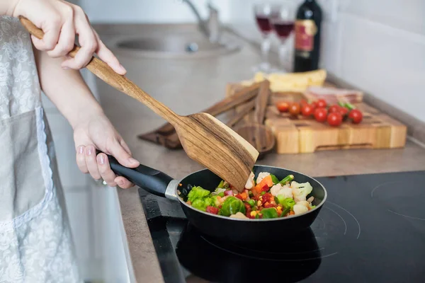 Meisje kookt groenten op het fornuis, roeren met een houten schop. Stockfoto