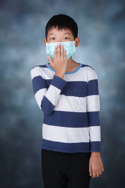 Asian boy Close the nose with mask to aviod PM2.5 on dark mood studio background.Asian child boy wearing a protection mask against PM 2.5 air pollution with pointing up in Bangkok city. Thailand. COPY.COVID-19