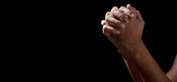 Man hands in praying position low key image. High Contrast isolated on Black Background. COPY SPACE.