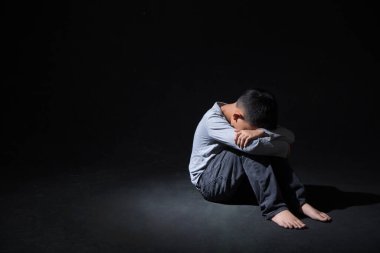 Asya 'lı Çocuk Kara Arkaplan' da dizlerinin üstüne çöküp oturuyor. Konsept: depresyonda. Hayal kırıklığına uğradım. Duygu. 