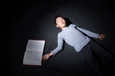 Asyalı Çocuk Kara Arkaplanda Ders kitabıyla Uyuyor. Konsept: depresyonda. Hayal kırıklığına uğradım. Duygu. Boşluğu Kopyala.