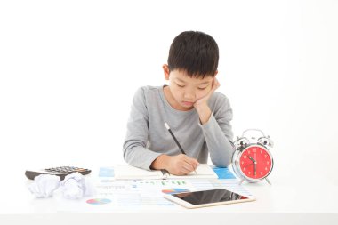 Küçük Asyalı çocuk beyaz arka planda gülümseyen yüzüyle deftere kalem yazıyormuş. Planlama Eğitimi Konsepti.