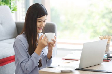 Mutlu, sıradan, güzel bir kadın. Dizüstü bilgisayarla çalışıyor. Evde yerde oturuyor..