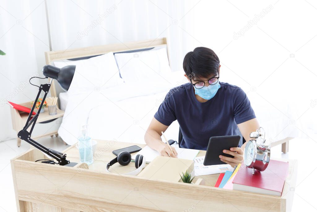 Serious man with Mask making note and checking on Paper Chart Report while sitting on Desk in the Bedroom. COPY SPACE. Trading. WORK FROM HOME WFH Concept.