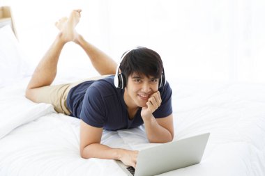 Mutlu adam dizüstü bilgisayar kullanıyor ve yatak odasındaki iyi haberleri kontrol ediyor. Kopyalama uzayı. Takas. Film izliyordum. Ev Konseptinden Çalışma.