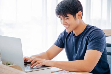 Mutlu Asyalı adam dizüstü bilgisayar kullanıyor ve iyi haberleri, ticareti, yatak odasında film izlemeyi kontrol ediyor. Kopyalama uzayı. Ev Konseptinden Çalışma.