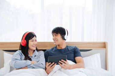Genç Asyalı sevimli çift, Tablet Bilgisayar kullanarak Mutlu Haber İzleme Filmini Yatak Odasında İzlerken. Birlikte vakit geçiriyorlar. Beyaz arka plan. Boşluğu Kopyalayan Erkek ve Kadın.