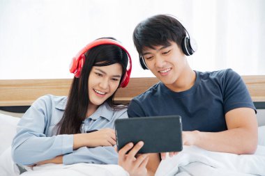 Genç Asyalı sevimli çift, Tablet Bilgisayar kullanarak Mutlu Haber İzleme Filmini Yatak Odasında İzlerken. Birlikte vakit geçiriyorlar. Beyaz arka plan. Erkek ve Kadın..