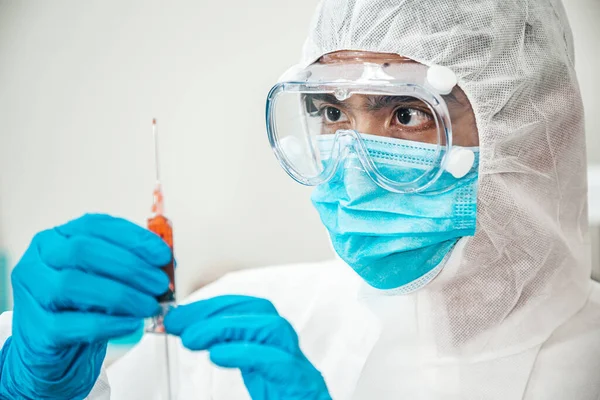 Koruyucu kıyafetli (PPE Suit) ve maskeli Asyalı bir adam şırınga ve aşı taşıyor. Grip aşısı, koronavirüs, ebola, tüberküloz. Biyolojik tehlike. Covid-19 salgını..