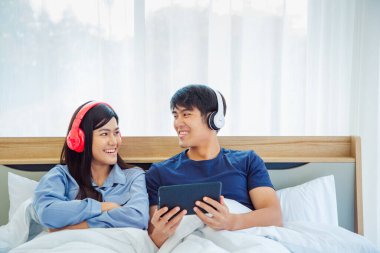 Genç Asyalı sevimli çift, Tablet Bilgisayar kullanarak Mutlu Haber İzleme Filmini Yatak Odasında İzlerken. Birlikte vakit geçiriyorlar. Beyaz arka plan. Erkek ve Kadın..