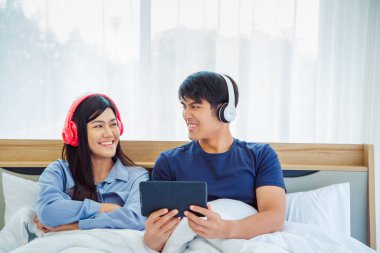 Genç Asyalı sevimli çift, Tablet Bilgisayar kullanarak Mutlu Haber İzleme Filmini Yatak Odasında İzlerken. Birlikte vakit geçiriyorlar. Beyaz arka plan. Erkek ve Kadın..