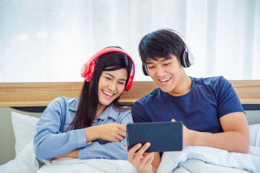 Genç Asyalı sevimli çift, Tablet Bilgisayar kullanarak Mutlu Haber İzleme Filmini Yatak Odasında İzlerken. Birlikte vakit geçiriyorlar. Beyaz arka plan. Erkek ve Kadın..