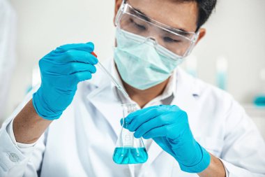 Erlenmeyer Matarası 'na çözüm dağıtırken laboratuvarda çalışan erkek bilim adamı. Tüp 'e odaklan. Mavi Ton. SARS-CoV-2, Covid-19 Teması.