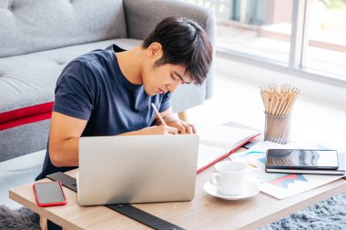 Oturma odasındaki masaya defter yazan ciddi bir adam. Kopyalama uzayı. Takas. Çalışıyorum. Ev Konseptinden Çalışma.