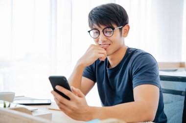 Masada cep telefonu kullanan mutlu Asyalı adam internette iyi haberler okuyor, Asyalı adam heyecanlanıyor zafer çığlığını sevinçle evde zaferi kutluyor. Ev Konseptinden Çalışma. 