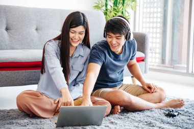 Genç Asyalı sevimli çift yatak odasındaki mutlu haberleri kontrol ederken dizüstü bilgisayar kullanıyor. Birlikte vakit geçiriyorlar. Erkek ve Dişi. Spor Maçı izlerken.