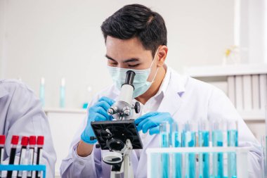Erkek Asyalı Bilim Adamı 'nın mikro mikroskop ile kan örneklerini kontrol edişinin yan görüntüsü. Hand ve Micro Scope lenslerine odaklan. SARS-CoV-2, Covid-19 Teması.