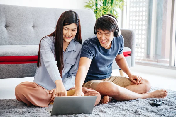 Genç Asyalı sevimli çift yatak odasındaki mutlu haberleri kontrol ederken dizüstü bilgisayar kullanıyor. Birlikte vakit geçiriyorlar. Erkek ve Dişi. Spor Maçı izlerken.