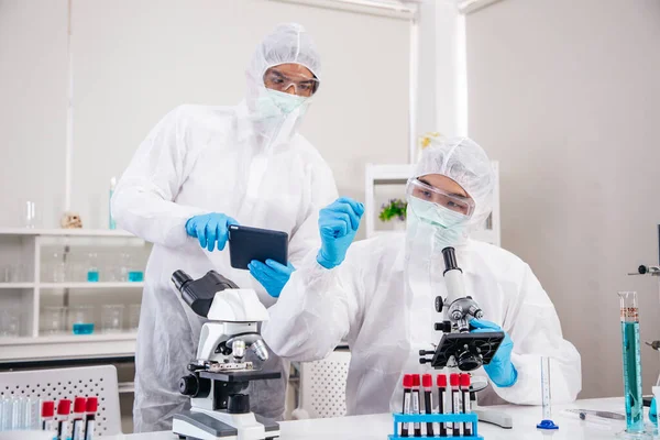 两名穿Ppe服的男性科学家在实验室工作 同时检查血液样本检测结果 蓝色调子Sars Cov Covid 19主题 免版税图库照片