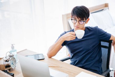 Yatak odasında kahve içerken masada defterle çalışan ciddi bir adam. Kopyalama uzayı. Takas. Çalışıyorum. Ev Konseptinden Çalışma.