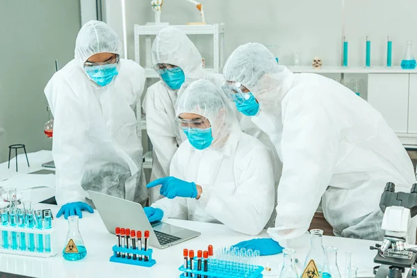 Group of Scientists wear Face Mask working in Lab while Checking Blood Sample by micro scope On Background.