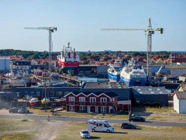 Skagen, Danimarka-13.08.2025: Turnaların altında büyük gemi ve balıkçı tekneleri, arka planda kırmızı evler ve liman binaları.