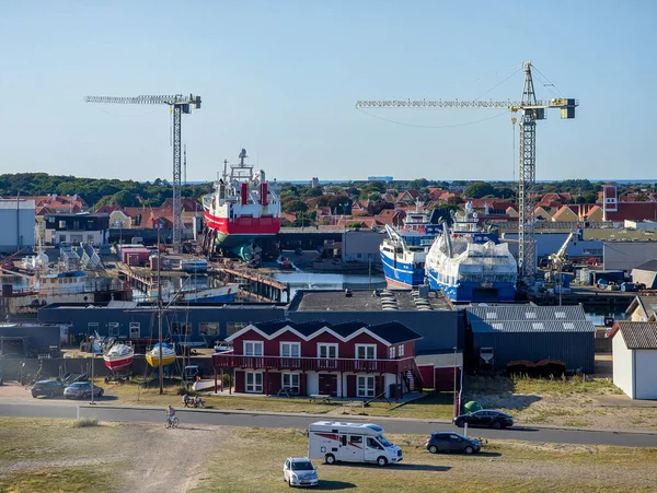 Skagen, Danimarka-13.08.2025: Turnaların altında büyük gemi ve balıkçı tekneleri, arka planda kırmızı evler ve liman binaları.