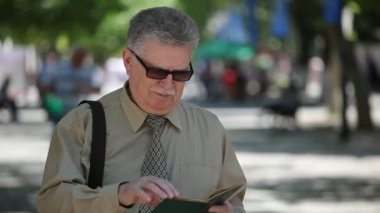 Üst düzey beyaz saçlı adam güneşli bir sokakta duruyor ve ayakta ve yaz aylarında pitoresk bir arka sokakta onun smartphone ile internette sörf mustashe ile mobil akıllı beyaz saçlı adam portresini net sörf