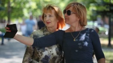 Mutlu anne ve kızı bir selfie duran ve yaz aylarında güneşli bir günde bir arka sokakta onun hayattan zevk şık bir bluz neşeli anne portresi yazında bir gree sokakta al. Sarışın kızı bir selfie alır