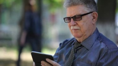 Komuta sizde cep telefonunu görünüyor ve yazın güneşli bir yaz aylarında yeşil bir sokakta oturan onun smartphone üzerinde net sörf bir kravat mustashe ile akıllı bir yaşlı adam portresi yeşil bir arka sokakta bilgi istiyor