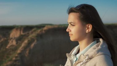 Beyaz kapüşonlu Atttractive kız beyaz kapüşonlu Karadeniz kıyısında duran ve günbatımı yaz aylarında bakarak uzun gevşek saç ile rüya gibi bir kızın yaz Closeup profilde batımında engebeli sahil üzerinde duruyor