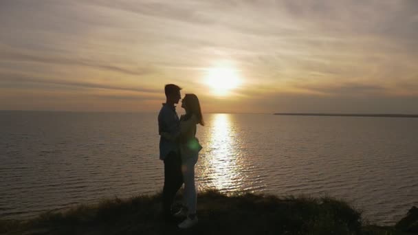 年轻夫妇拥抱彼此浪漫的黑海海岸在日落的轮廓一个美丽的年轻女子拥抱她浪漫的男朋友在黑海海岸上灿烂的日落与金色的太阳路径在夏季 — 图库视频影像