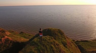 Cesur bir adam Karadeniz sahilinde keskin bir tepe üzerinde günbatımında inanılmaz bir kuşbakışı göz pan bir mürettebat saç kesimi ve yeşil bir tepede güneş gözlüğü ile sportif bir adam ayakta ve altın güneş yol günbatımında gözlemleyerek hava