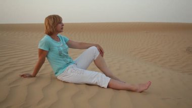 Kumlu deniz kıyısında yaz aylarında sanatsal bir şekilde oturan güzel sarışın kadın profili sahil üzerinde oturan bir romantik ve zarif sarışın kadının çöl dunes ile kaplı. Tek bacak gerilir, ikinci bir bükülmüş