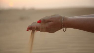 Şık eller tutun ve parlak makyaj yaz aylarında altın bir gün batımı, deniz kıyısı dunes üzerinde sarı kum taneleri eleme ile etkileyici bir manzara güzel kadının el tatlı Dubai güneş ışınları altında kum elemek