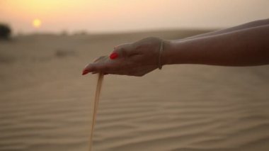 Güzel eller tutmak ve kum sahil dunes üzerinde altın bir günbatımı güzel kadının elleri inanılmaz bir görünümünü çölde kum bir avuç tutmak ve Dubai'de parıldayan bir günbatımında düşmesini izin kırmızı makyaj ile elemek 