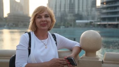 Neşeli sarışın kadın ile Uluslararası Dubai Kongre ve Sergi Sarayı yaz yaz aylarında güneşli bir günde bir su kanalı çit Burj Dubai Dubai onun arkasından ayakta gülümseyen bir backpacker kadın portresi onun arkasından gülümsüyor 