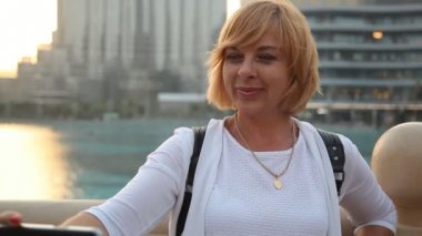 Turistik kadın bir selfie ile Uluslararası Dubai Kongre ve Sergi Sarayı arka planda yaz bir selfie alarak ve neşeyle bir su kanalı, onun arkasından duran Uluslararası Dubai Kongre ve Sergi Sarayı ile gülümseyerek mutlu bir sarışın kadın portresi alır 