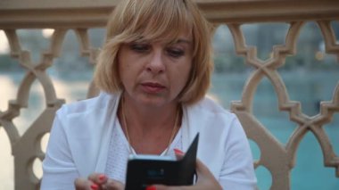 Akıllı sarışın kadın oturur ve telefonunu yüzme havuzunda oturuyor ve onun smartphone vasıl yaz aylarında bir çit ile çevrili yüzme havuzu net tarama şık bir sarışın kadın portre, net sörf
