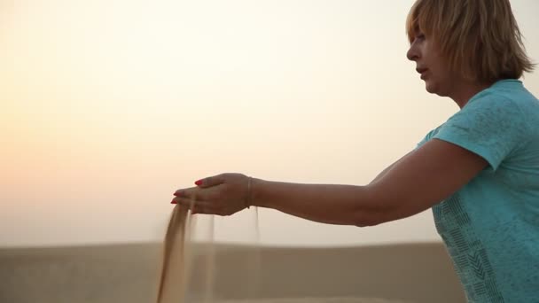 一个活泼的女人在迪拜风景如画的海滨 在夏天的金色夕阳下 在迪拜的一个黄色海岸上 用双手筛选沙子 在一个美丽的沙滩上筛沙子 海被看见遥远的 — 图库视频影像