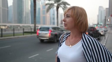 Karayolu ile gökdelenler Dubai profilinde bir beyaz T-shirt, kot pantolon ve yaz aylarında güneşli bir günde, otoyol Dubai Mr.Right için bekleyen bir çizgili pelerin içinde şık bir kadın, erkeğini kendine güvenen kadın bekler