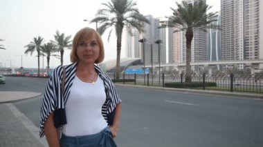 Ayakta ve zarif bir kadın ayakta ve mutlu bir şekilde avuç içi Dubai ile modern bir otoyol yaz aylarında güneşli bir gülümseyen neşeli bir görünümünü karayolu Dubai avuç içi ile gülümseyen şık kadın turist