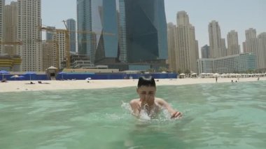 On yaşındaki çocuk Dubai yeşil sularda slo-mo güneşli bir atlama ve ayak ilk ışık yeşil dalgalar halinde Dubai kum plajındaki slo-mo yaz aylarında dalış neşeli bir küçük çocuk iyimser bir bakış atlar